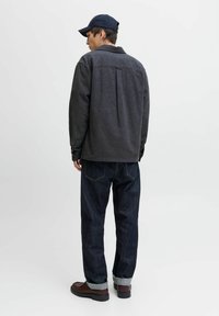 Chaqueta gris de mezcla de lana con cuello y pliegue en la parte posterior, combinada con jeans de mezclilla azul oscuro y zapatos marrones, vista desde la parte de atrás.