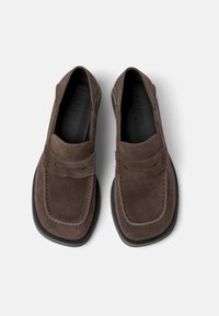 Brown suede loafers with a square toe and a stitched detail on the front. Black rubber sole; minimalist design without visible hardware.