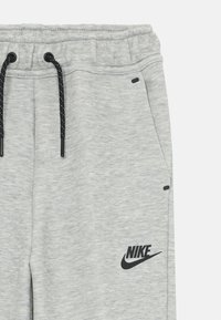 Sive trenerke iz mehkega materiala, z vrvico za nastavljanje, stranskimi žepi in črnim logotipom Nike na levem stegnu.