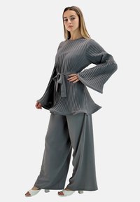 Top gris plisado con amplias mangas acampanadas, combinado con pantalones grises holgados. Presenta un cinturón de lazo a juego para mayor detalle.