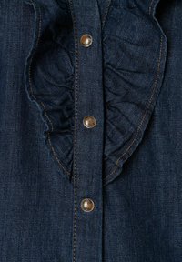 Camicia di denim scuro con dettagli arricciati lungo la patta, bottoni in metallo e cuciture arancioni in contrasto.