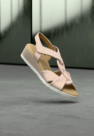 Sandale rose blush avec un design à brides croisées, texture douce, petit talon compensé et semelle en caoutchouc blanc, sur un fond neutre.