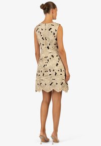 Beige bloemen kant jurk met een aansluitende silhouet, mouwloos ontwerp, geschulpte zoom en een verborgen rits aan de achterkant. Gemaakt met doorzichtige hakken.
