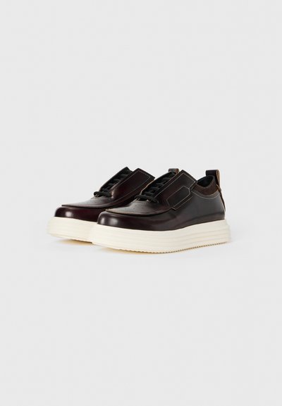 Chaussures en cuir bordeaux foncé avec une semelle blanche épaisse, un bout rond, une plateforme surélevée et des lacets noirs. Elles présentent une texture lisse et des accents minimalistes.