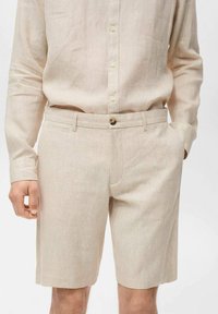 Linen shorts in light beige with a button closure, flat front, and side pockets; knee-length design with a textured fabric finish.
