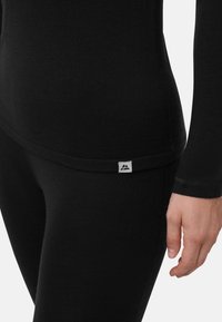 Schwarzes, sportliches Langarm-Oberteil mit glatter Textur und figurbetontem Design. Verfügt über ein kleines Logo-Etikett am Saum. Betont die Körperform.