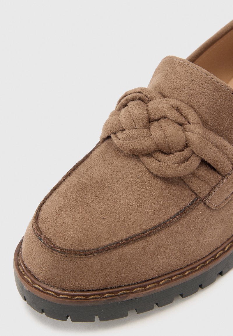 Mocassino in suede marrone con dettaglio annodato, punta tonda e cuciture a contrasto, dotato di suola in gomma testurizzata con pattern antiscivolo.