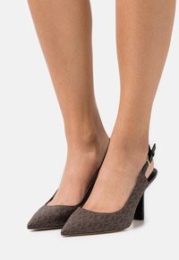 Talons slingback marron avec des bouts pointus, tissu texturé avec un motif géométrique, et un design de talon épais. Sangle réglable avec boucle.