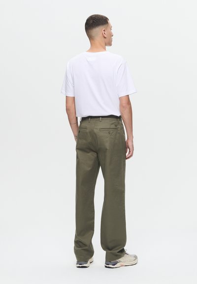 Pantalons larges vert olive avec une texture lisse, deux poches arrière et un logo brodé. Associés à un t-shirt blanc uni et des baskets.