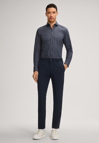 Camicia blu navy con bottoni e un sottile motivo bianco, abbinata a pantaloni blu navy e sneakers bianche. Tessuto liscio, design slim fit.