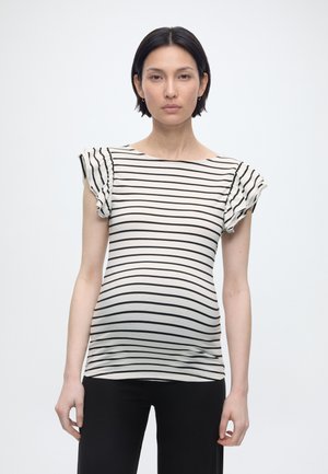 Έγκυος γυναίκα με κοντά μαύρα μαλλιά στέκεται απέναντι φοράει λευκό τοπ με μαύρες οριζόντιες ρίγες και κοντά βολάν μανίκια.