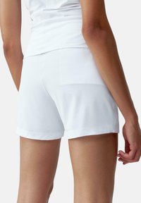 Pantalones cortos blancos de tela suave, con corte ajustado, dobladillo limpio y detalles de costura mínimos, mostrando la vista trasera y una textura natural.