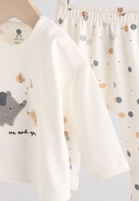 Conjunto de algodón blanco con camiseta de manga larga que presenta un diseño texturizado de erizo y texto "yo y tú"; pantalones a juego con lunares en colores pastel.