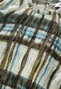 Bluza cu mâneci scurte din material ușor, texturat, cu dungi verticale albastre, verzi și maronii; are detalii adunate de-a lungul cusăturilor.