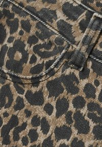 Jeansfiber i leopardmönster med en beige och svartdesign, med framträdande sömmar och en fickdetalj. Strukturerad yta.