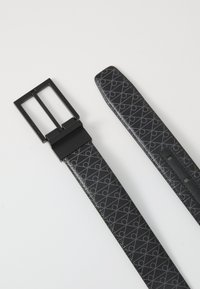 Svart belte med et mønsterdesign, prydet med en rektangulær, matt svart spenne og flate ender. Teksturen er glatt og litt blank.