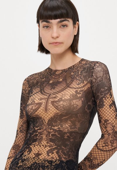 Prozirni top s dugim rukavima s intrikatnim čipkastim uzorcima, cvjetnim detaljima i križnim motivom u crnoj boji na nude pozadini. Glatka tekstura.
