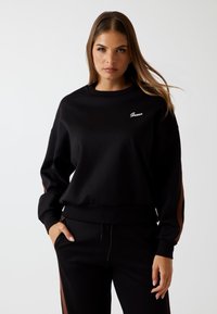 Felpa nera con vestibilità rilassata, caratterizzata da un collo rotondo, polsini a costine e un logo bianco sul petto a sinistra; texture liscia.