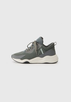 Baskets de sport grises avec dessus en mesh, lacets à l’avant, semelle blanche rembourrée et languette au talon, présentées en vue latérale sur un fond uni.