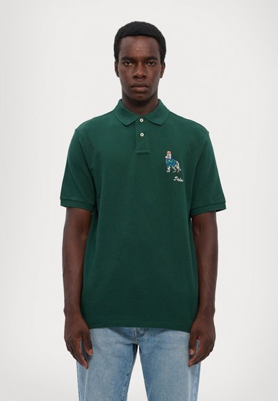 Cămașă polo verde închis cu guler, două butoane și mâneci scurte. Include un design brodat cu un câine și textul "Polo".