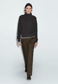 Maglione a collo alto a coste scuro con dettagli sulle spalle, abbinato a pantaloni dritti verde oliva. Dettaglio a righe all'orlo del maglione.
