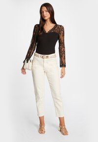Zwarte bodysuit met lange kanten mouwen, gecombineerd met roomkleurige rechte broek en een beige tas. Opvallende riem met gouden accenten en sandaaltjes met bandjes.