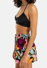 Svart bikiniöverdel med volangdetaljer och tunna axelremmar, i kombination med flerfärgade shorts med blommönster och dragsko i midjan.