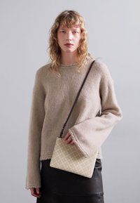 Un pull en laine beige avec des manches larges, assorti à un petit sac à main matelassé de couleur claire présentant un motif en diamants.