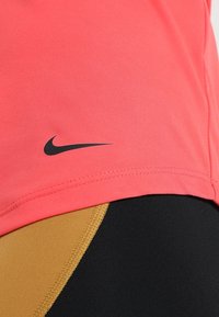 Nike-Sportshirt aus leuchtend pinkem Material mit einem schwarzen Logo auf dem linken Ärmel. Kombiniert mit schwarzen und sandfarbenen Leggings. Glatte Textur.
