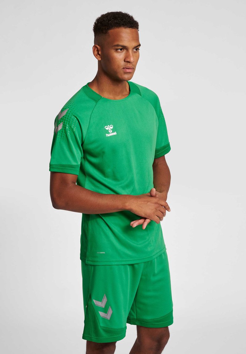 Grön sporttröja och shorts tillverkade av andningsbart tyg, med en logotyp och grå chevronmönster på shortsen.