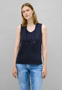 Top senza maniche di colore blu navy con scollatura a V e cordino regolabile. Tessuto morbido e liscio in vestibilità rilassata, abbinato a jeans in denim azzurro chiaro.