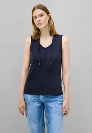 Marinefarbener ärmelloser Oberteil mit V-Ausschnitt und verstellbarem Kordelzug. Weiche, glatte Textur in einer lockeren Passform, kombiniert mit hellblauen Jeans.