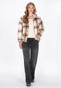 Ruudullinen takki tan, valkoinen ja ruskea, napilla edessä, päällä vaaleanbeige paita. Yhdistetty mustiin leveälahkeisiin farkkuihin ja mustiin saappaisiin.