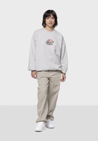 Felpa grigia oversized con un design grafico multicolore sul davanti, abbinata a pantaloni cargo beige a gamba larga e sneaker bianche.