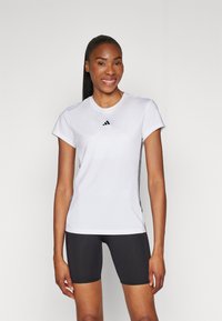 Valge lühikeste varrukatega sportlik t-särk, millel on Adidas logo rinnal. Kandmise alla on mustad kitsad lühikesed püksid, mis on siledast materjalist.