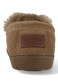 Bruine suède pantoffel met een ronde achterkant, voorzien van een pluizige bontafwerking, gestikte details en een gestructureerde rubberen zool. Merketiket zichtbaar.