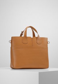 Tan leren shopper met twee handvatten en een gladde textuur. Heeft een eenvoudig ontwerp met horizontale stiksels en een vlakke basis.