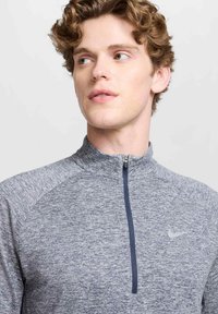Grijsharige atletische shirt met ritssluiting, vervaardigd uit een gestructureerde stof, met een marineblauwe ritssluiting en het Nike-logo op de borst.