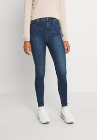 Jeans ajustados en denim azul oscuro con una textura suave. Diseño de cintura alta con bolsillos tradicionales y detalles de costura sutiles.