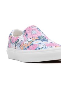 Baskets à enfiler florales avec un fond blanc orné de motifs de fleurs roses, oranges et bleues. Semelle en caoutchouc avec adhérence texturée. Tissu léger.