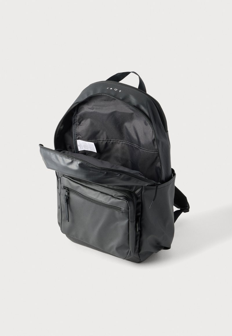 Black backpack with one main compartment open, showing interior pocket and fabric tag, and a front zippered pocket on a plain background.