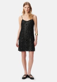 Vestito in pizzo nero con un motivo circolare a strati, spalline sottili, taglio a ginocchio, abbinato a scarpe basse nere. Gli accessori includono gioielli metallici.