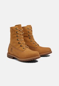 Bottes en cuir tan avec texture en daim, bout rond et design à lacets. Comprend des œillets métalliques et une semelle en caoutchouc avec traction. Logo sur le côté.