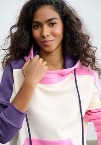 Bluza z kapturem o kremowym korpusie, fioletowych rękawach i różowych akcentach. Gładki materiał z troczkiem i prążkowanymi mankietami.