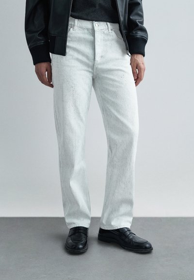 Jean blanc droit avec une finition texturée, taille haute et poches avant, associé à des mocassins noirs.
