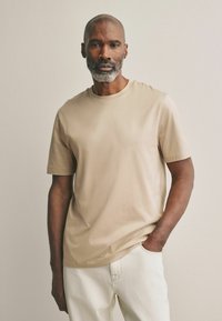 Camiseta de manga corta beige en tejido suave con cuello redondo clásico, con un corte relajado y un diseño minimalista sin patrones.