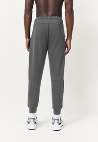 Gray sweatpants with an elastic waistband, tapered legs, and side pockets, paired with white and blue athletic shoes.