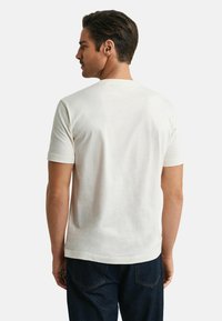 Hvid bomulds t-shirt med korte ærmer, rund hals og en glat tekstur, båret med mørkeblå jeans, set fra ryggen.