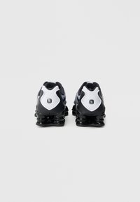 Černo-bílé tenisky s elegantním designem, vybavené gumovou podrážkou, síťovaným svrškem a jemným logem na patě.