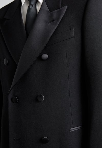 Melns divrindu uzvalka žakets ar zīda atloku, matētām pogām un vienu krūšu kabatu. Tekstūrēts audums ar gludu apdari.